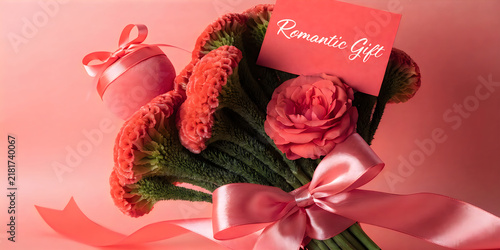 Coral celosia flower bouquet with pink satin ribbon and romantic gift card on pink surface.