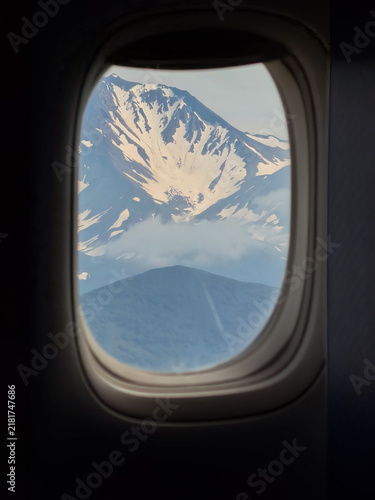 Konstfotografi Snow-covered volcano rises above clouds, seen through airplane window during flight over Kamchatka