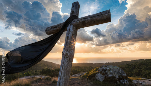 Wooden cross draped with black fabric at sunset symbolizing mourning and spirituality on hilltop.