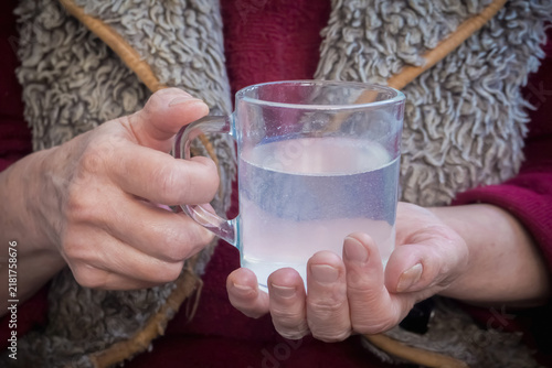 Elderly woman hands holding a glass mug with dissolved effervescent medicine liquid
