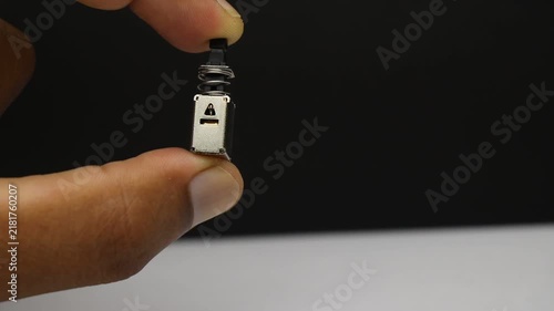 Switch component held in fingers showing the spring loaded button used to turn a circuit on or off with a single press