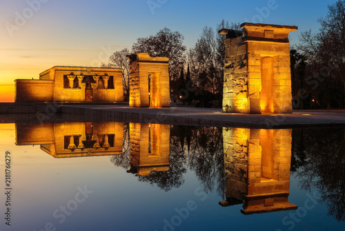 Egyptian Temple of Debod lit up at golden hour with clear reflection on calm water in Madrid park during sunset