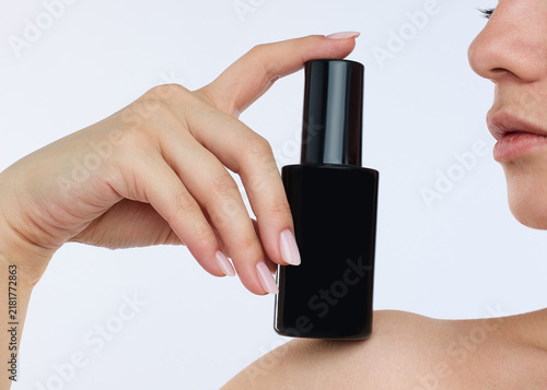 a woman with a perfect manicure holds a black jar on a light background