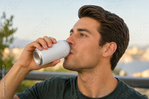 Close up of man drinking from a blank white aluminum can outdoors. Image with copy space.