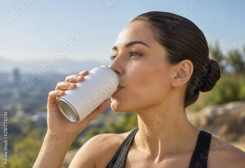 Close up of young athletic woman drinking from a blank white aluminum can outdoors. Image with copy space.