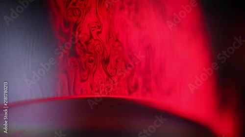 Crimson red liquid film wall with intricate marbling and dark curved horizon. A low-key macro photograph featuring a vertical liquid film surface glowing with intense crimson red light.