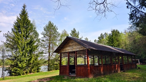 Foto There is a wooden gazebo with a slate roof and a long wooden table and benches on the grassy lawn