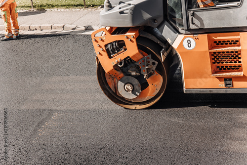 Fotografía Orange road roller compactor smoothing fresh asphalt pavement close-up