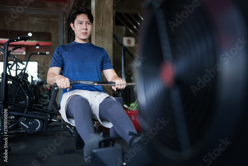Foto Young Asian man exercising on rowing machine during cardio workout in modern fit