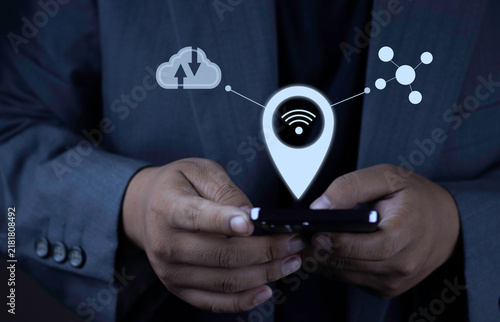 Foto Cloud computing and mobile work anywhere concept with businessman operating smartphone displaying location pin wifi, cloud data transfer, and network node icons on dark background