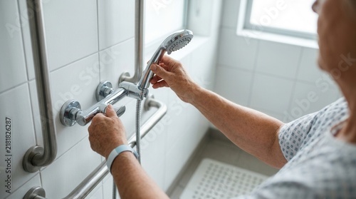 Elderly person adjusting shower head in a disabled-friendly bathroom with grab bars, promoting independence and assisted living.