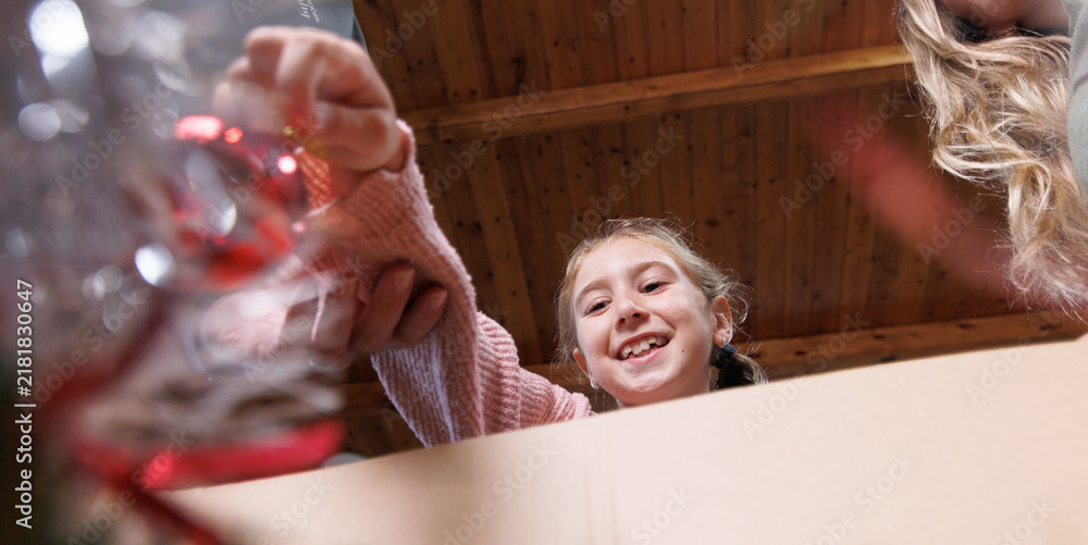 Obraz premium A girl smiles as she takes a Christmas ornament out of a box