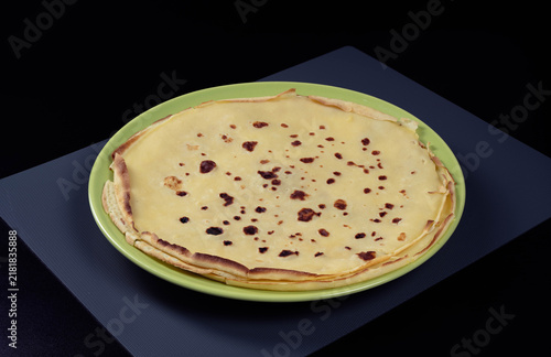 Stack of homemade crepes with golden brown spots served on green plate, dark background
