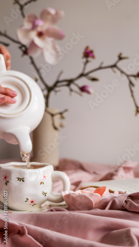Картината върху платно Pouring tea into a delicate floral mug with magnolia branches in the background