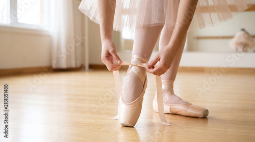 Graceful ballet dancer tying pink pointe shoe ribbons before practice perfect for professional classical dance preparation and artistic dedication