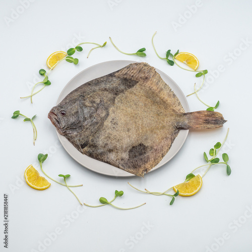 Fotografie Fresh raw flounder fish on a plate with lemon slices, top view