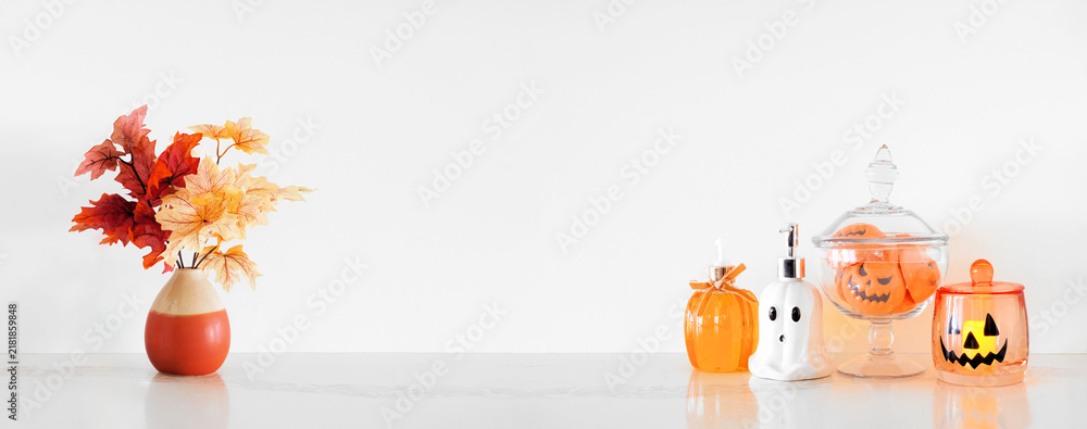 Obraz premium Halloween pumpkin and ghost theme body care on a white stone countertop. Banner against a white wall background with copy space. Bathroom decor concept. Soaps, lotion, bath fizzers.