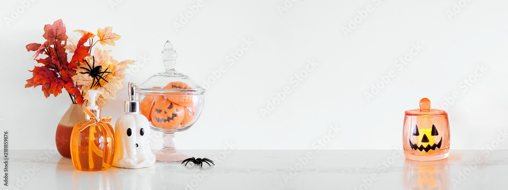 Obraz premium Halloween pumpkin and ghost theme body care on a white stone countertop. Banner against a white wall background with copy space. Bathroom decor concept. Soaps, lotion, bath fizzers.