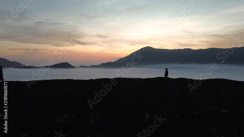 Silhouette of a man and woman meeting and embracing on a hill above the clouds at dawn