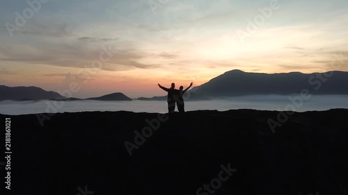 Young couple in silhouette raising their arms and celebrating on a mountain top above the clouds
