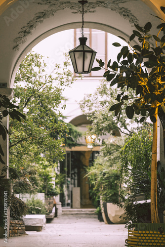 Fotografie Elegant European courtyard with lush green plants, hanging lantern and arched pa