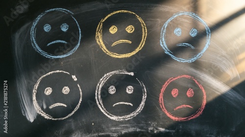 Sad face icons drawn with colorful chalk on a dark blackboard background
