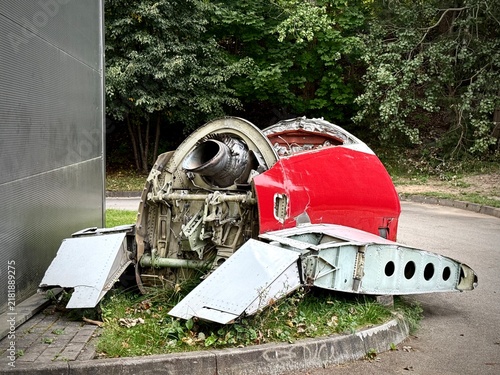 Canvas Print Horizontal photo of discarded red aircraft wreckage, showing an exposed jet engine exhaust nozzle, internal mechanisms, and aluminum wing panels beside an industrial building
