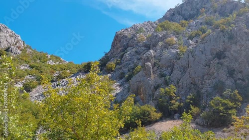 A horizontal, eye-level panning shot showcases the rugged, majestic limestone cliffs and lush green valley of Paklenica National Park in Croatia under a vibrant blue sky on a bright summer day