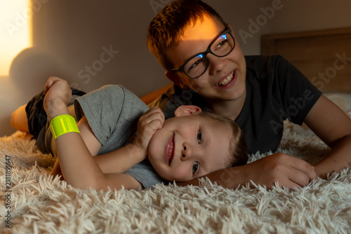 Happy older brother embracing his younger sibling as they rest together on a fluffy bed. Concept of brotherly love, protection, family unity, secure attachment and positive mental health in childhood.