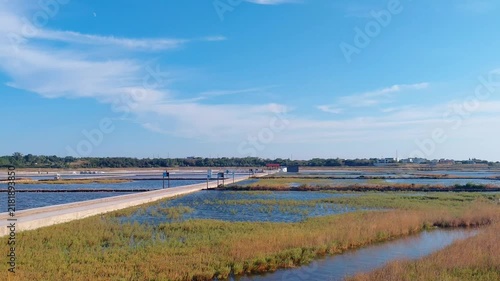Panoramic scenic view of the historic salt pans and wetlands at Solana Nin in Croatia. Evaporation basins, concrete pathways, and lush aquatic vegetation under a clear blue sunny sky in Dalmatia.