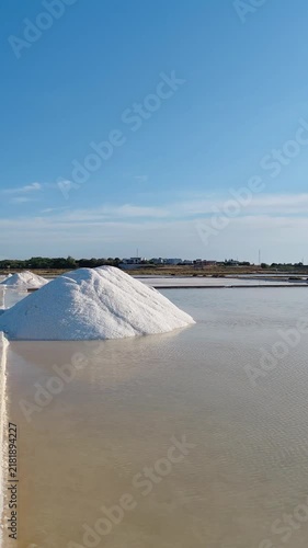Mound of harvested white sea salt in an evaporation basin at Solana Nin, Croatia. Calm shallow saltwater pool, concrete path, and blue sky at historic sea salt works along the Dalmatian coast.