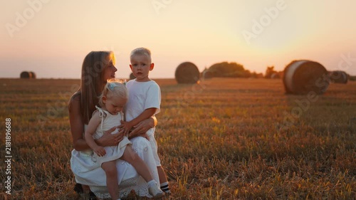 Loving mother embracing her young children in a golden harvested field at sunset, enjoying peaceful family time together in warm summer countryside light