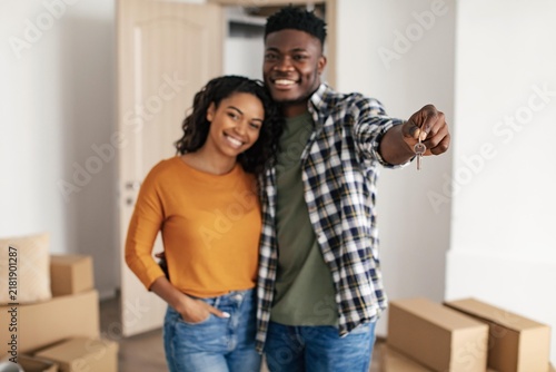 Foto Smiling Black Couple Holding New Home Keys Together In Living Room Surrounded By Cardboard Boxes, Celebrating Their New Beginning
