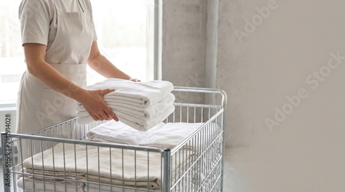 Person in apron loading folded white linens into wire laundry cart