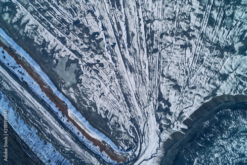 Fotografie Snowy eroded slag heap slopes with frozen drainage stream and dark mineral veins
