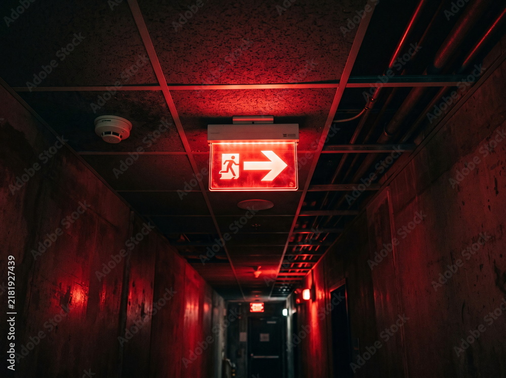 Fototapeta premium Illuminated Red Exit Sign in Dark Hallway Corridor