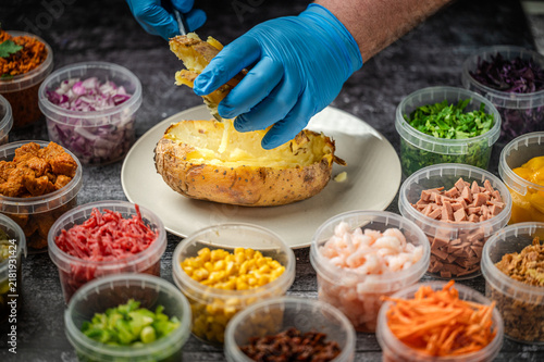 Baked potatoes with cheese, herbs, meat and butter. Copy space background. BBQ or steakhouse side dish favorite with tomato beans, cheddar cheese, bacon.