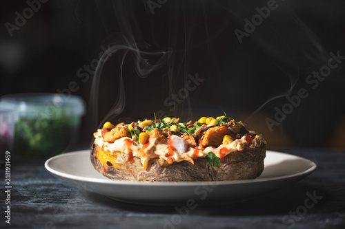 Baked potatoes with cheese, herbs, meat and butter. Copy space background. BBQ or steakhouse side dish favorite with tomato beans, cheddar cheese, bacon.
