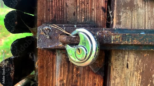 Shiny stainless steel disc padlock locking a rusty metal latch on an old wooden door.
