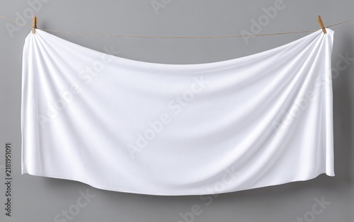 A pristine white fabric hangs from a twine line against a neutral gray backdrop, exhibiting soft, gentle folds