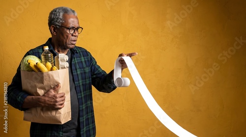 Shocked senior man holding grocery bag and looking at long receipt