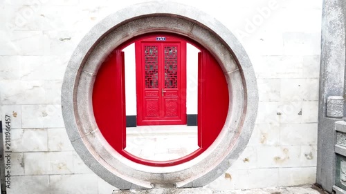 Traditional moon gate entrance and red wooden lattice doors at a historic Chinese temple in Cholon, Ho Chi Minh City, Vietnam