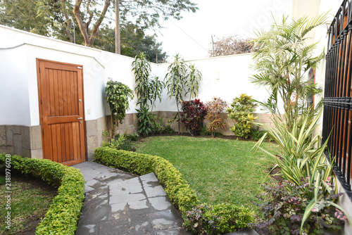 Serene Backyard A meticulously landscaped private backyard features a lush green lawn, manicured hedges, and diverse tropical plants, creating a tranquil escape with a charming wooden door.