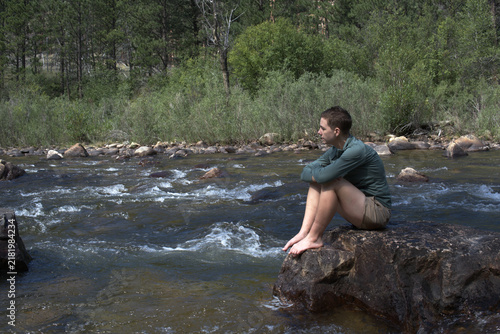 Fotografie In deep thought a woman sits on a rock in the river contemplating modern stress