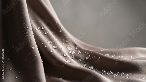 Water droplets and crystals on draped taupe satin fabric