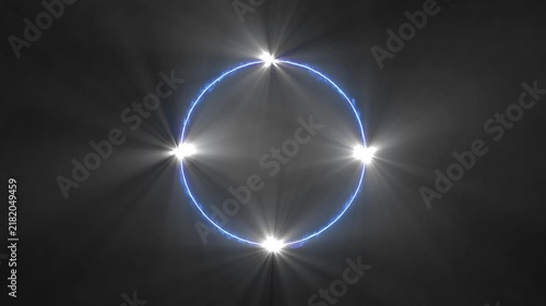 A bright blue circular neon ring with four intense white starbursts at cardinal points set against a smoky dark gray background with subtle light rays and atmospheric haze Keywords: blue, neon