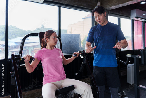 Foto Young Asian woman training with male fitness coach on shoulder press machine in