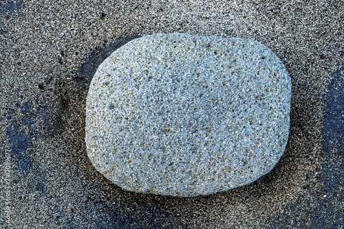 Photography Smooth grey stone lying on wet beach sand top view, minimal natural texture background close-up