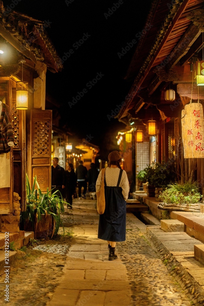 Obraz premium Woman walking away down lantern-lit alley at night, Shaxi Ancient Town, Yunnan, China