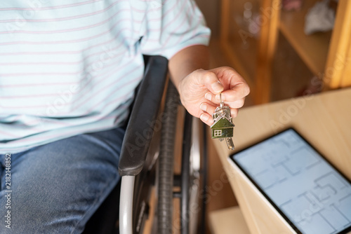 Konstfotografi Person in a wheelchair holding keys with a house-shaped keychain, symbolizing ho